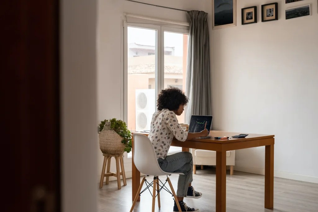 Woman sitting at a desk in a home office looking at her computer screen.