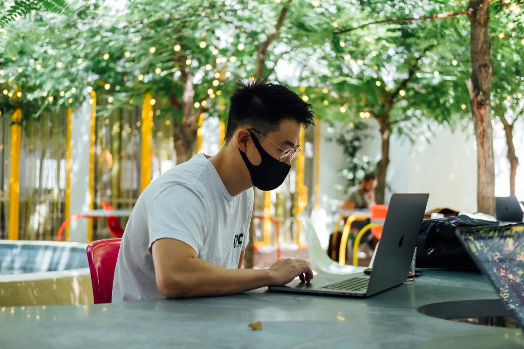 Man sitting at a table outdoors looking at a laptop.